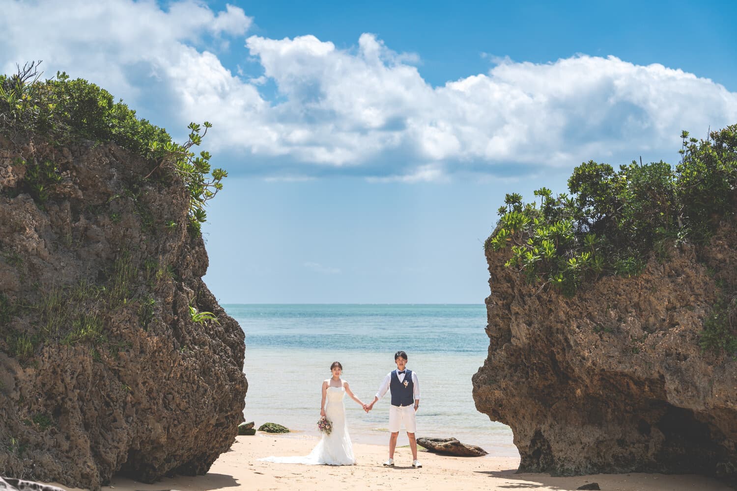 海を背景に岩場の間に手を繋いで立つ新郎新婦