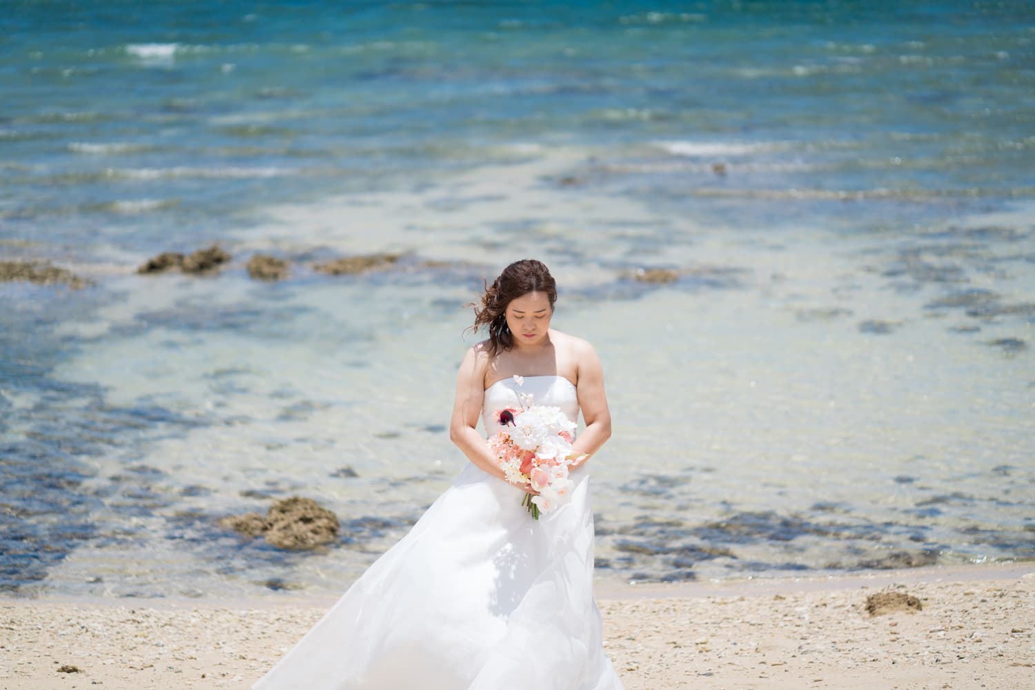 海を背景にブーケに視線を落とす新婦