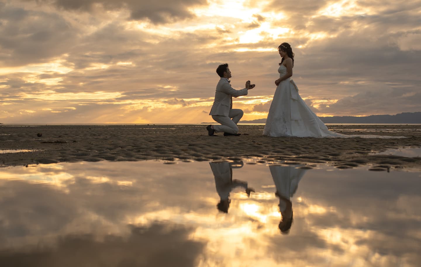 夕焼け空の海で新婦へプロポーズする新郎