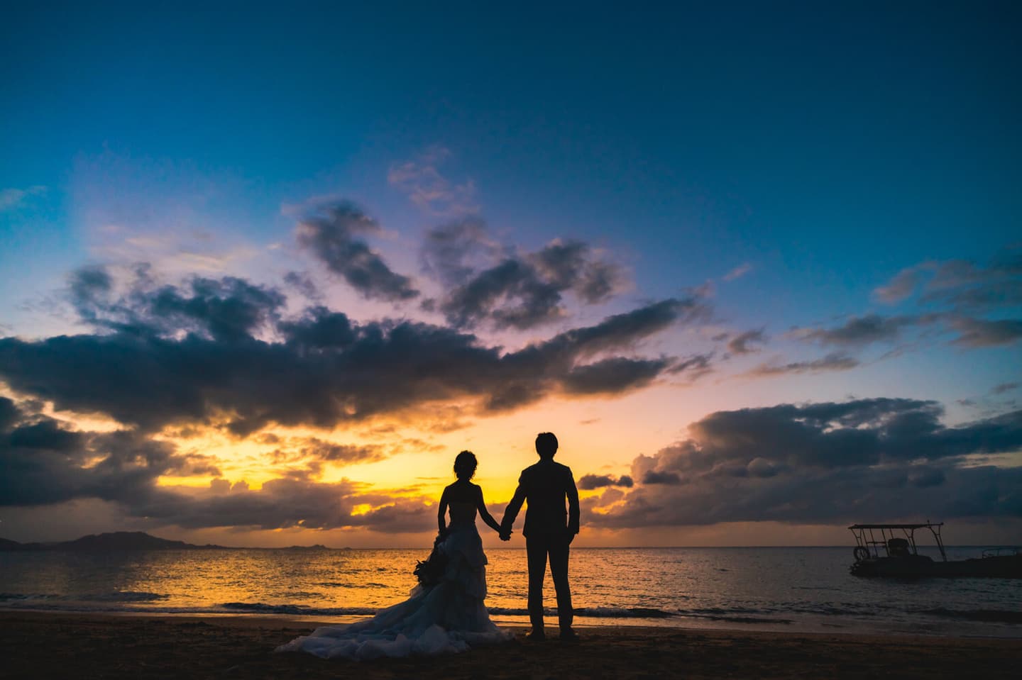 夕焼けに染まる海を眺める新郎新婦の後ろ姿