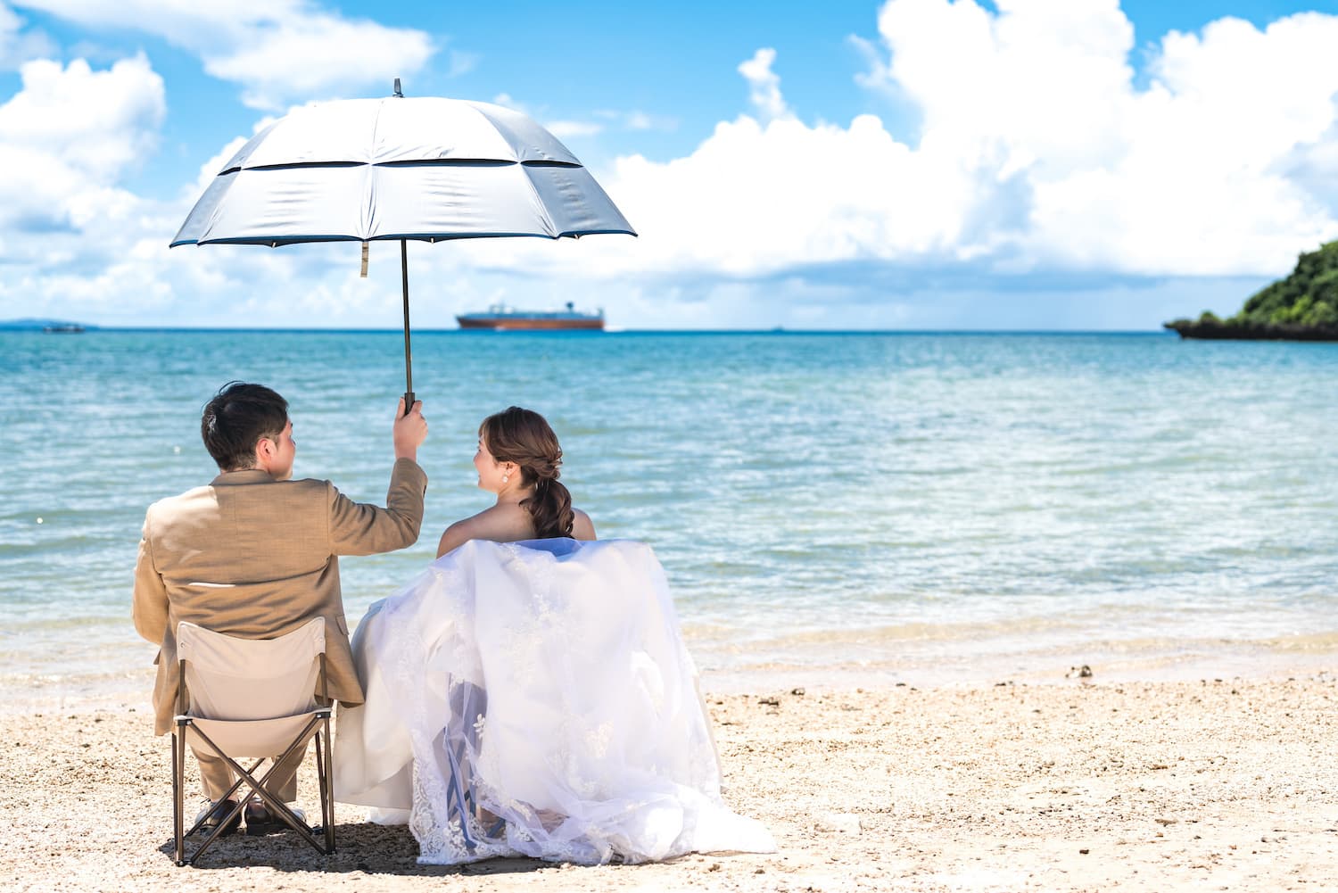ビーチで椅子に座って日傘をさす新郎新婦