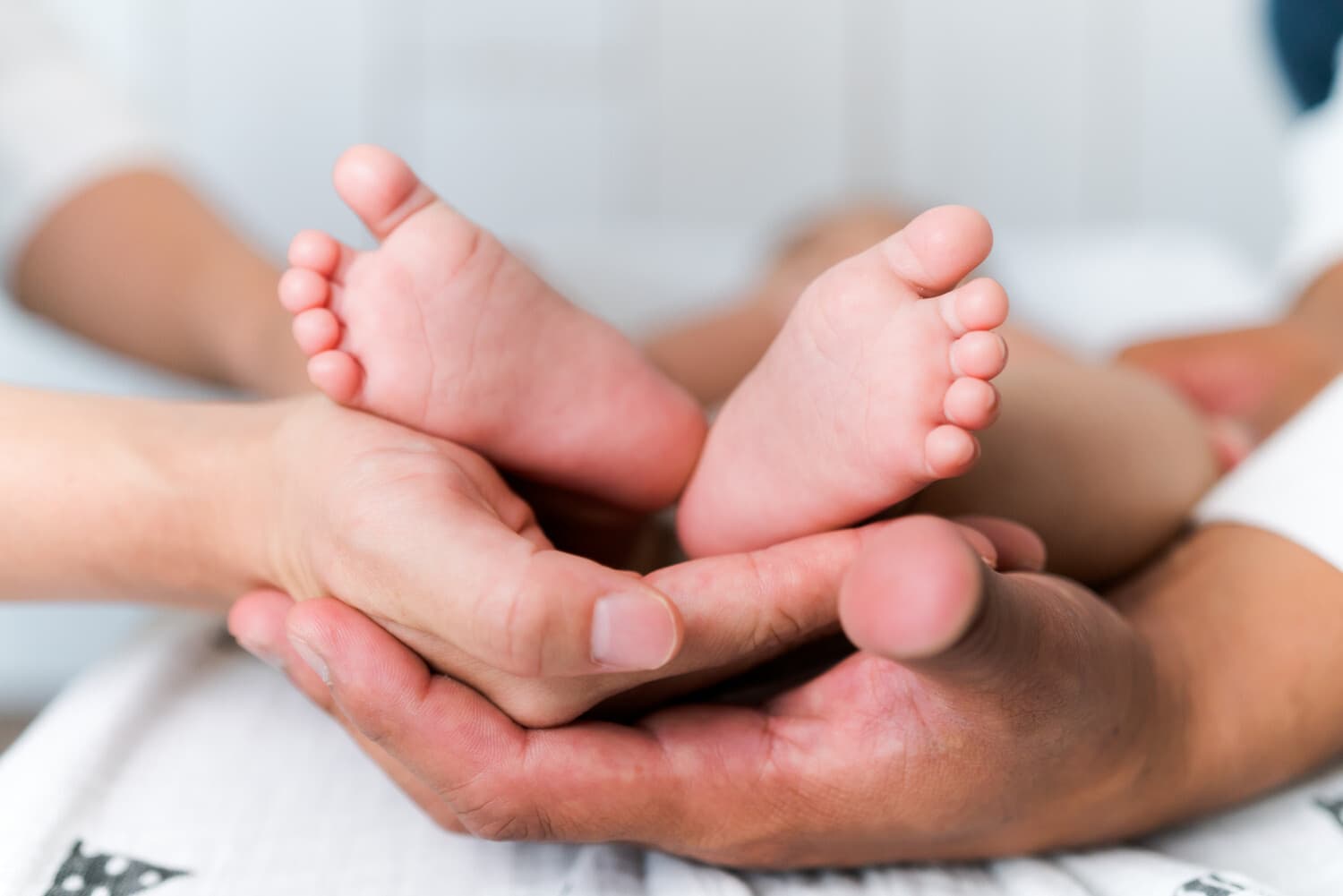 小さな赤子の足に手を添える父と母の手元
