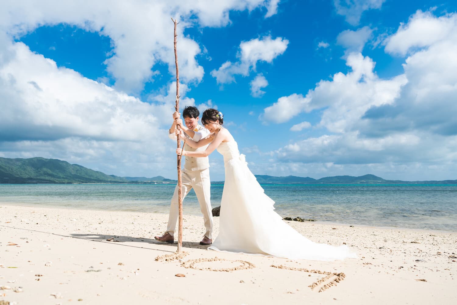 石垣島の浜辺に流木で文字を刻む新郎新婦