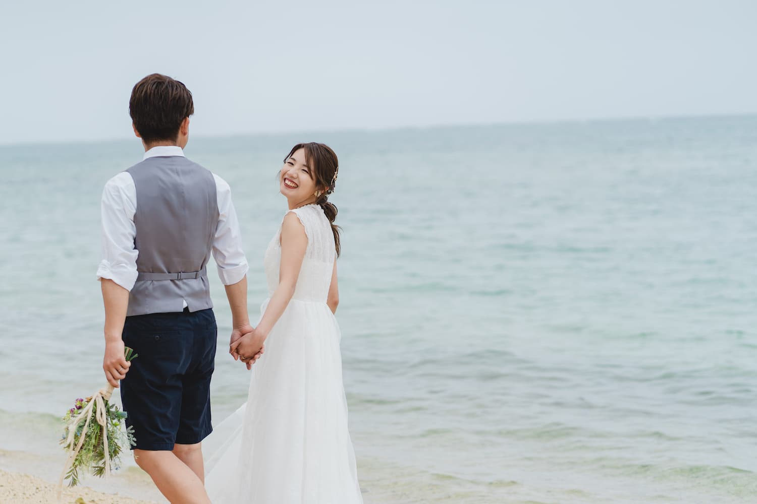 石垣島の海を背景に手を繋いで歩く新郎新婦