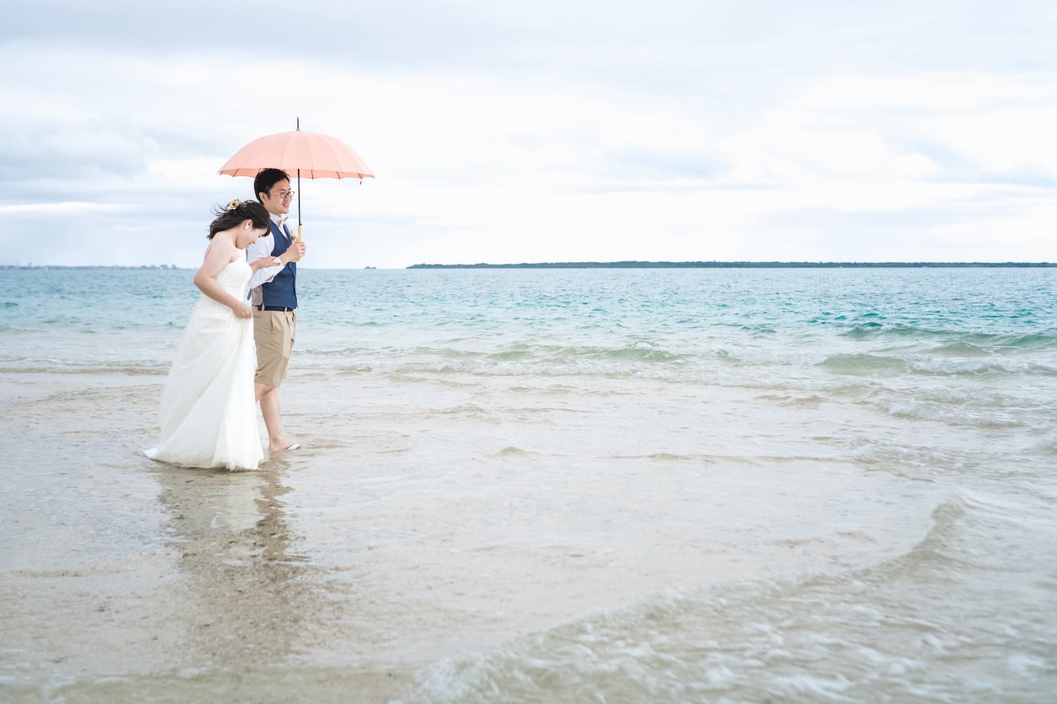 幻の島で海に足を踏み入れ傘をさしている新郎新婦