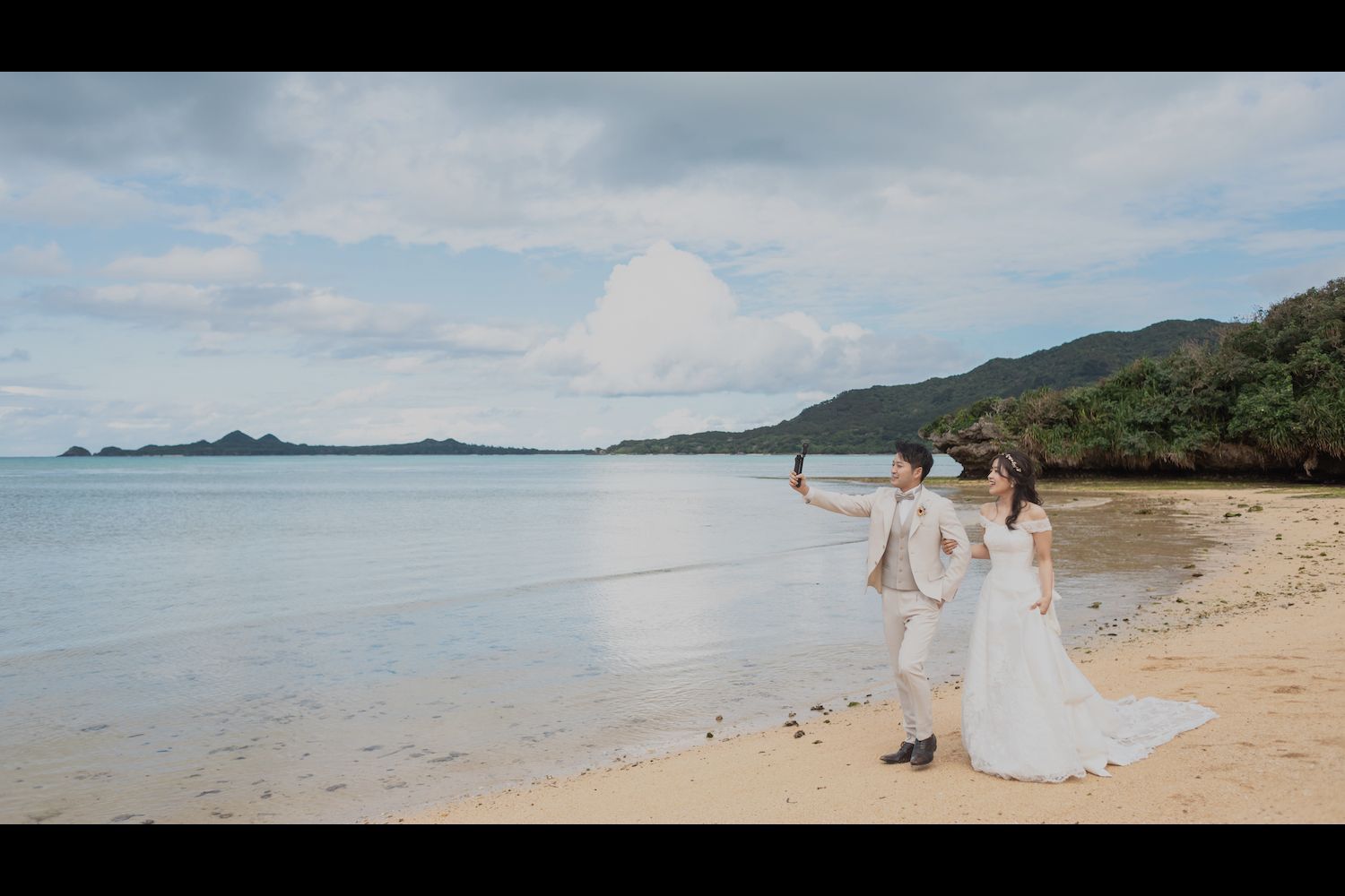 石垣島のビーチで動画を撮りながら歩く新郎新婦