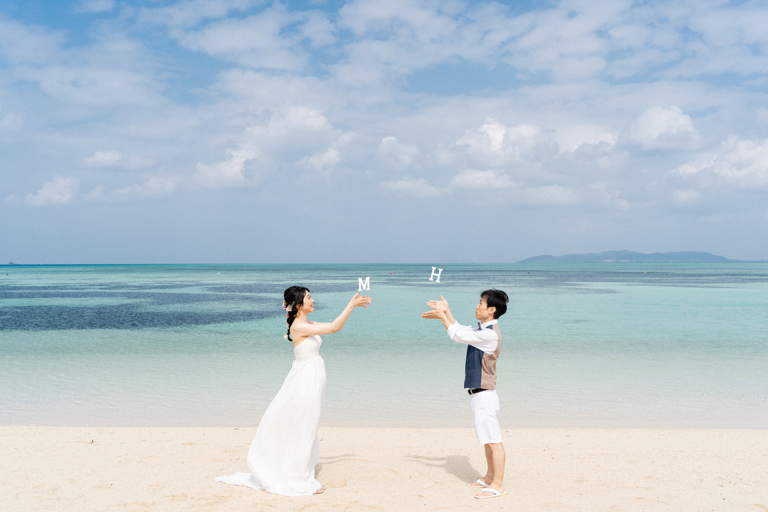 竹富島の海を背景にイニシャルブロックを宙に浮かせる新郎新婦