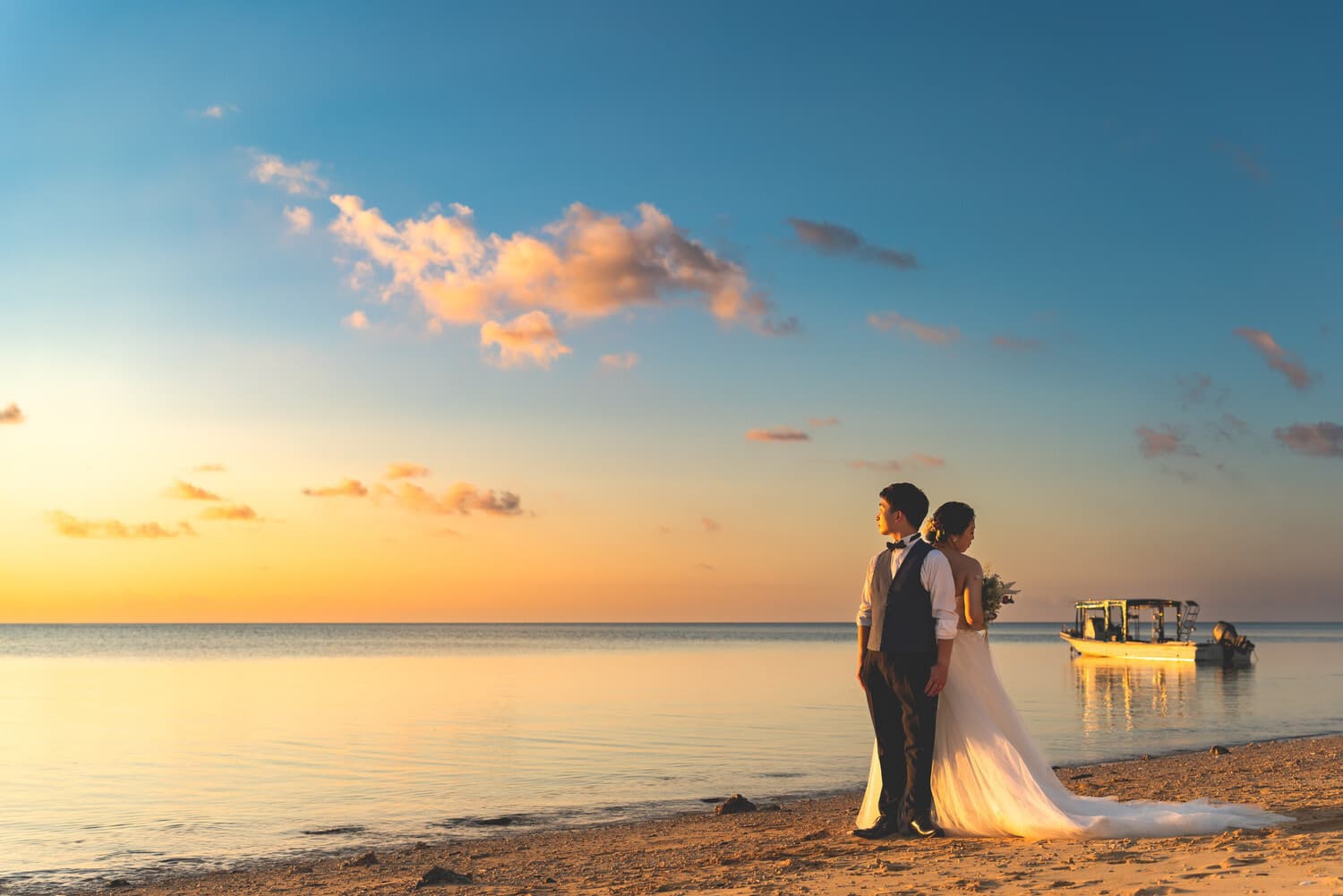 夕焼けの海を背景に背中合わせに立つ新郎新婦