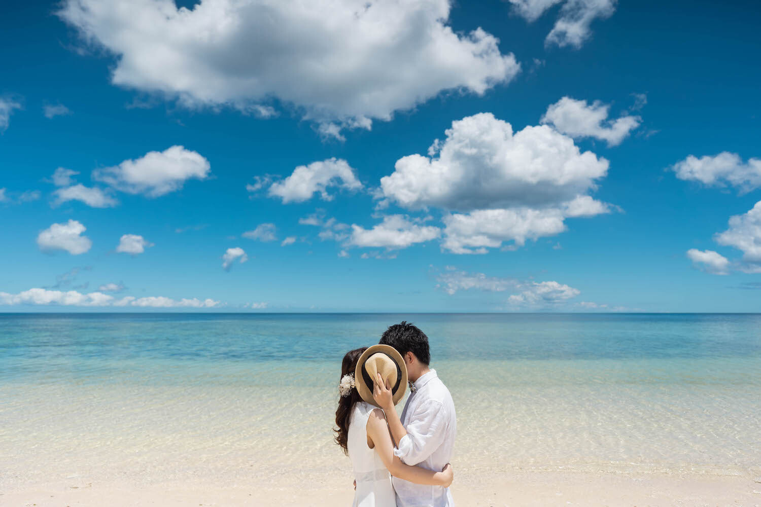 石垣島の青い海を背景に帽子で顔を隠す新郎新婦