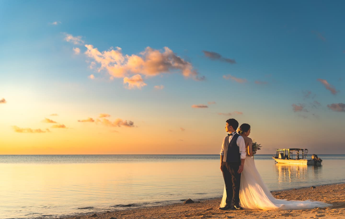 夕焼けに染まる海を背景に背中合わせに立つ新郎新婦