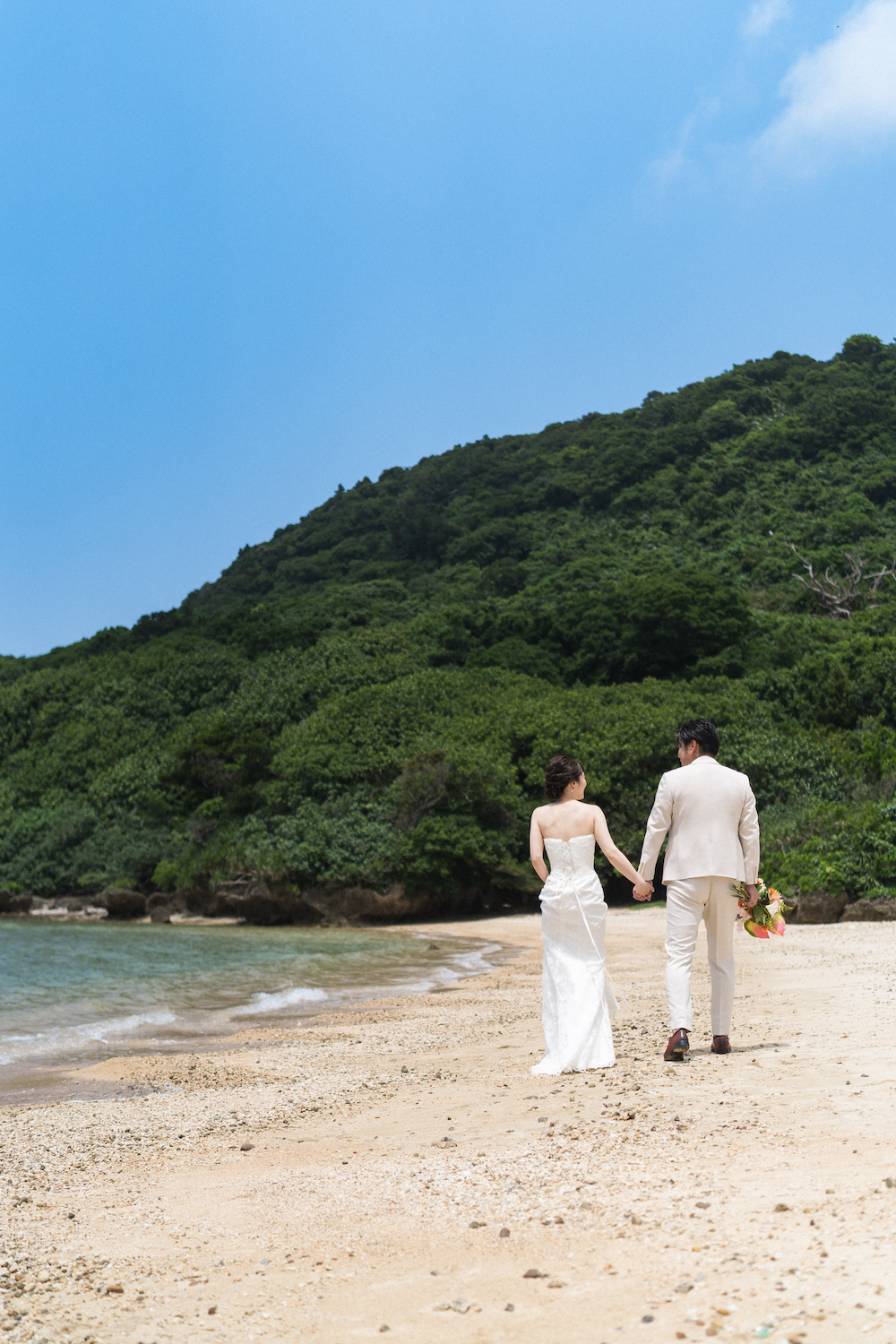 石垣島の浜辺で手を繋いで歩く新郎新婦の後ろ姿