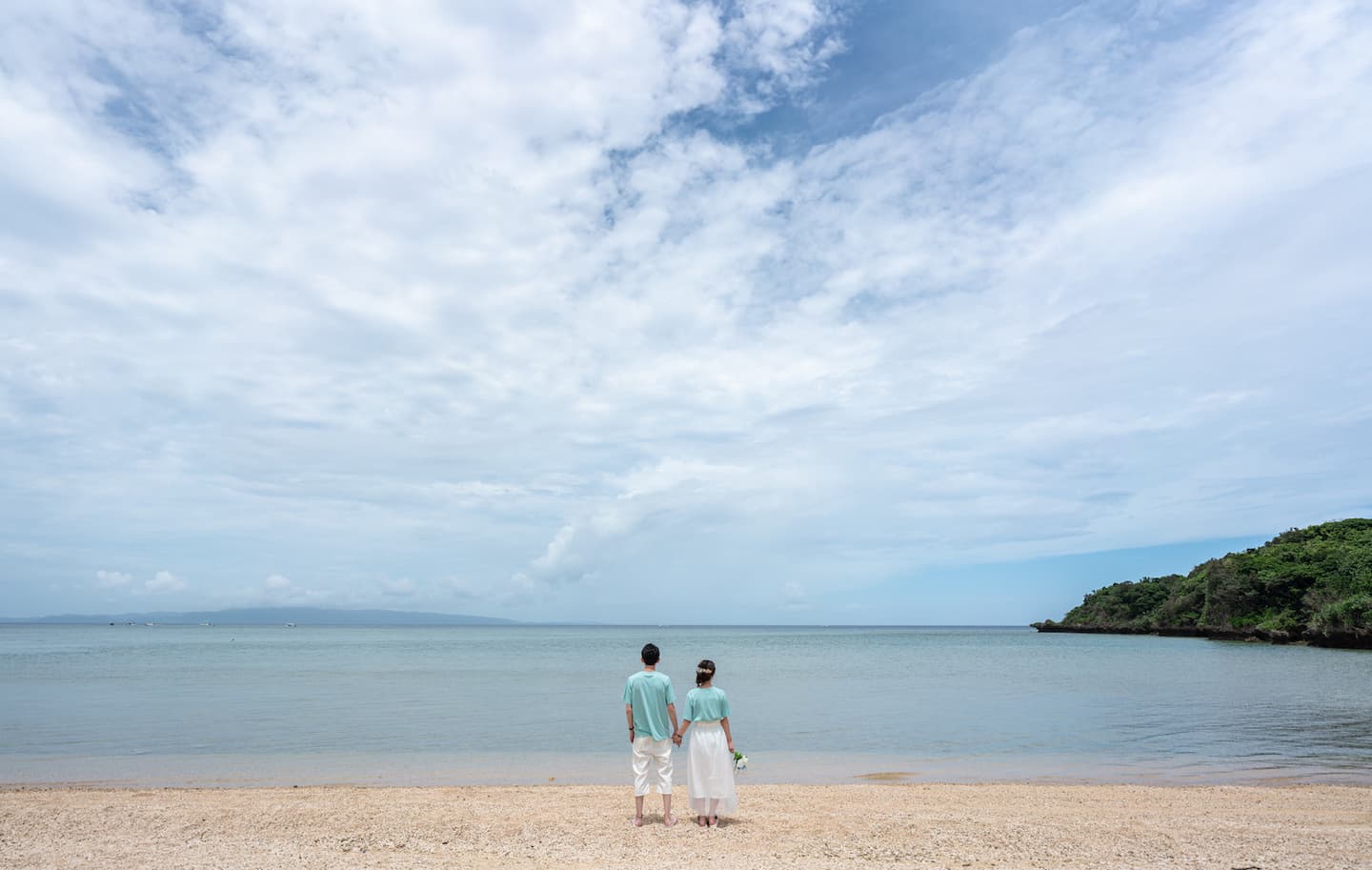 おそろいのTシャツで海を眺める新郎新婦の後ろ姿