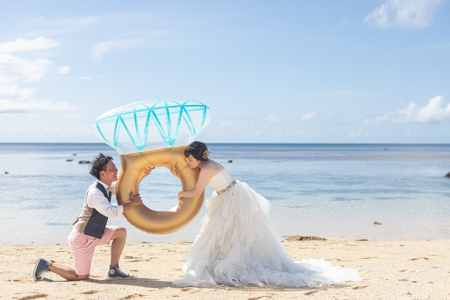 海を背景に大きなリングのバルーンを持つ新郎新婦