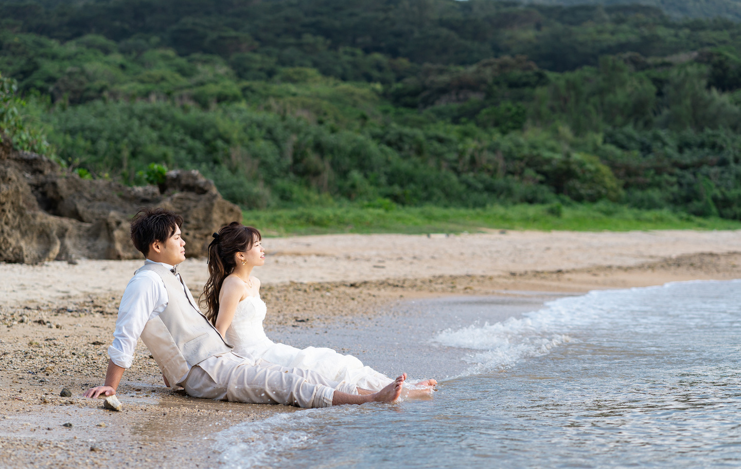 波打ち際に座って海を眺める新郎新婦