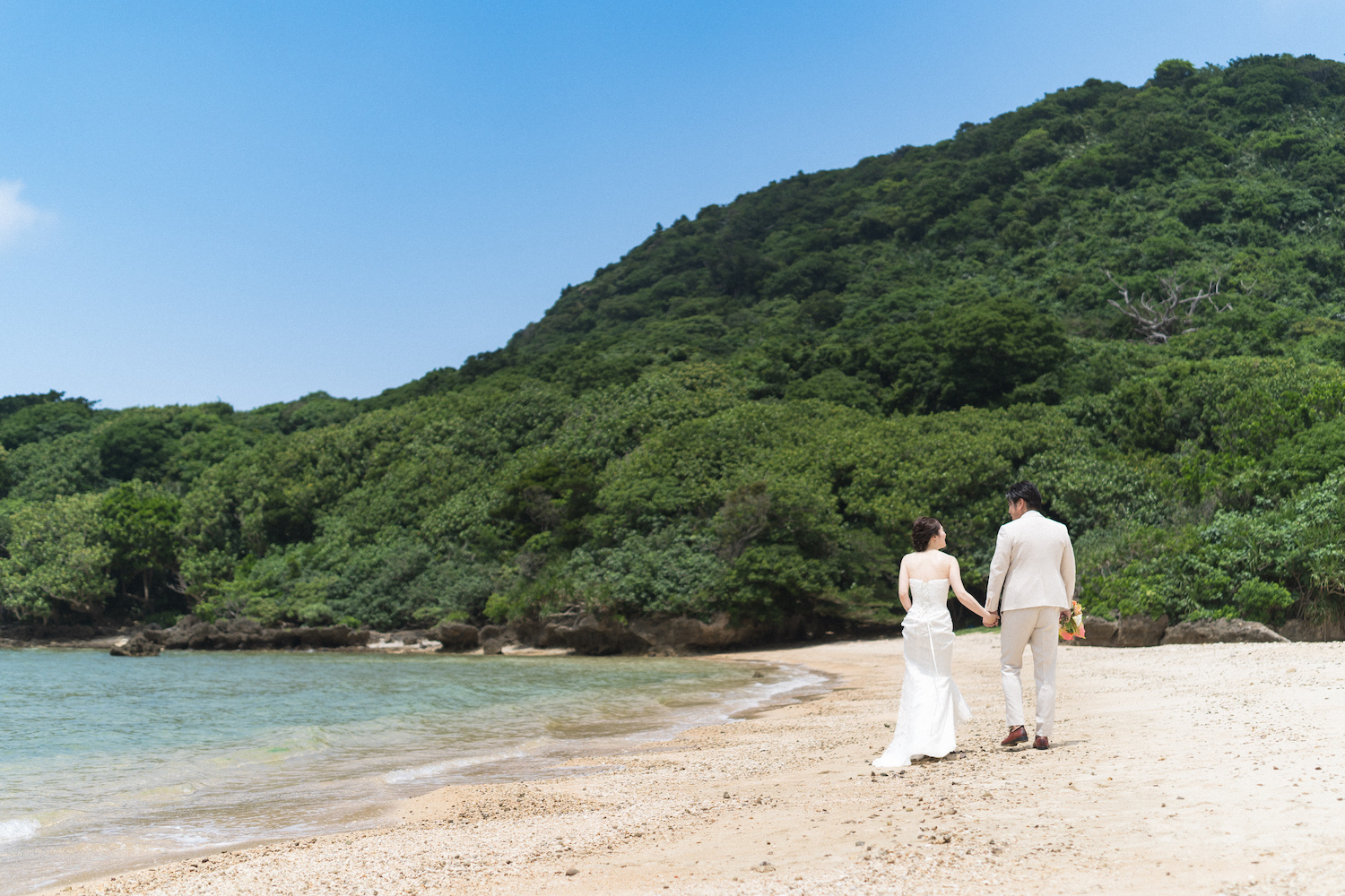 手を繋いで浜辺を歩く新郎新婦の後ろ姿