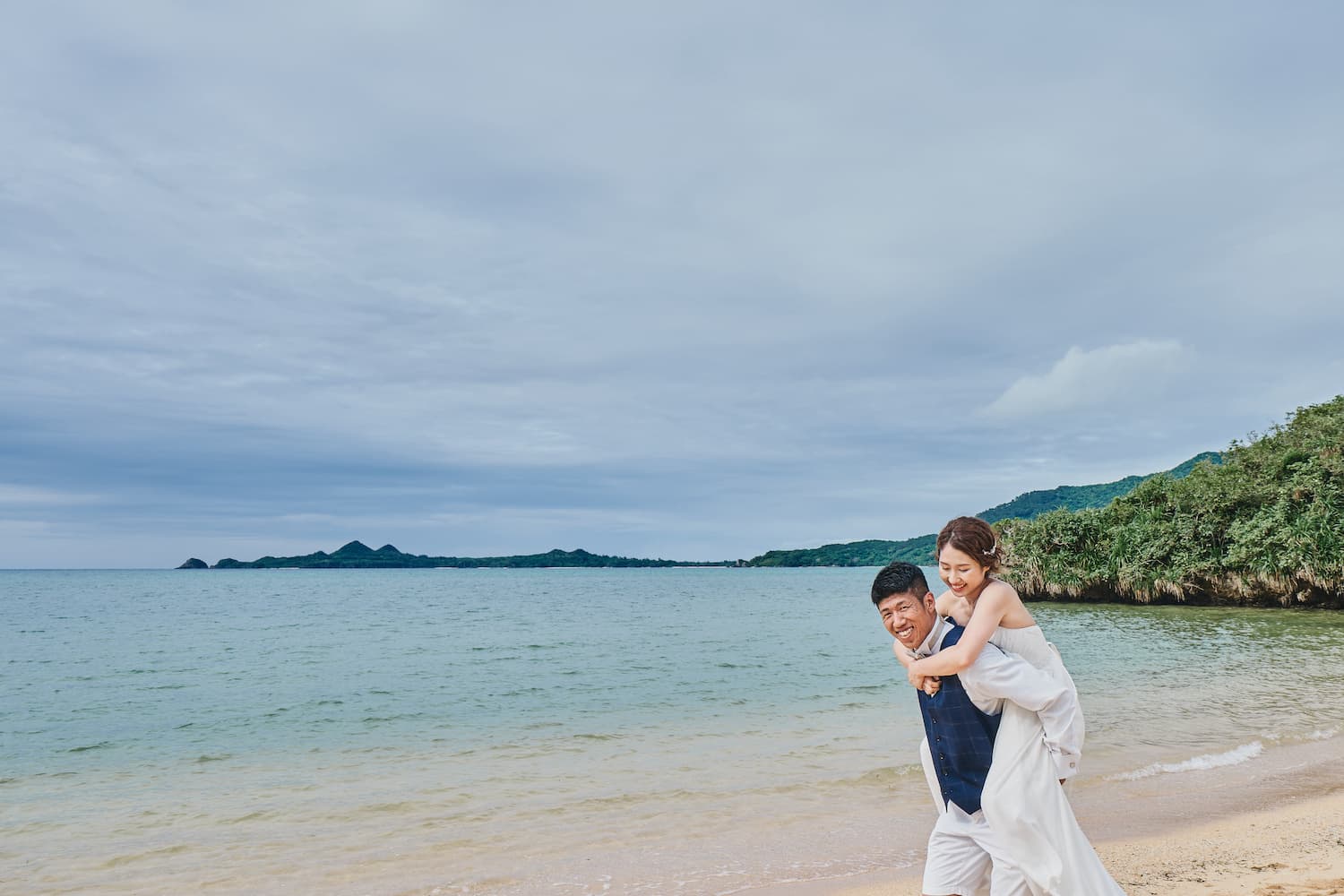 海を背景に新婦をおぶう新郎