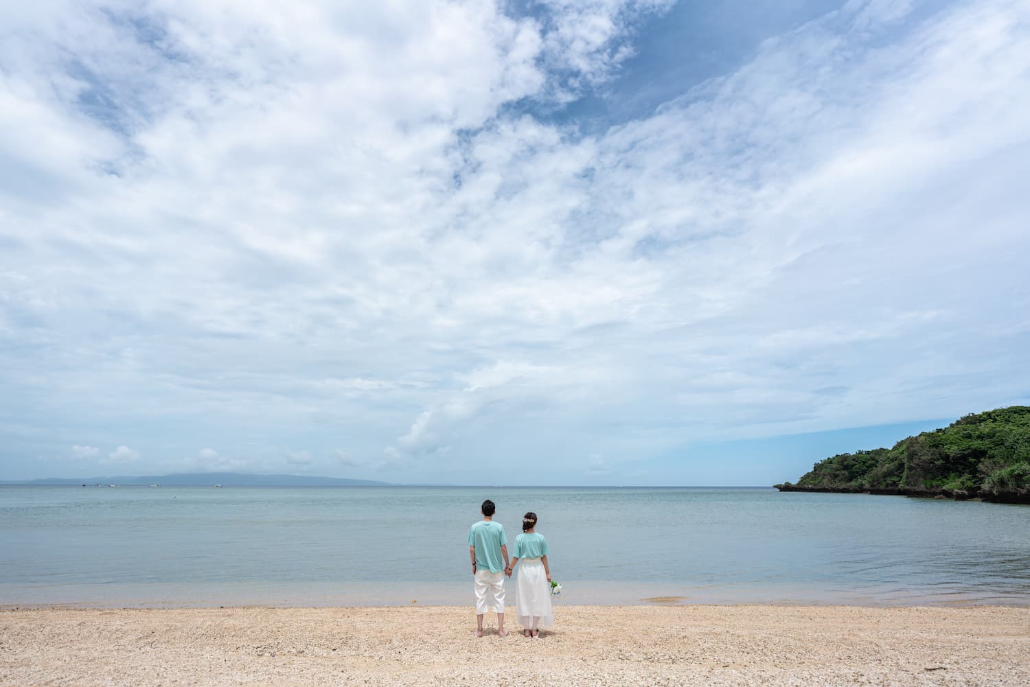 お揃いの服で海を眺める新郎新婦の後ろ姿