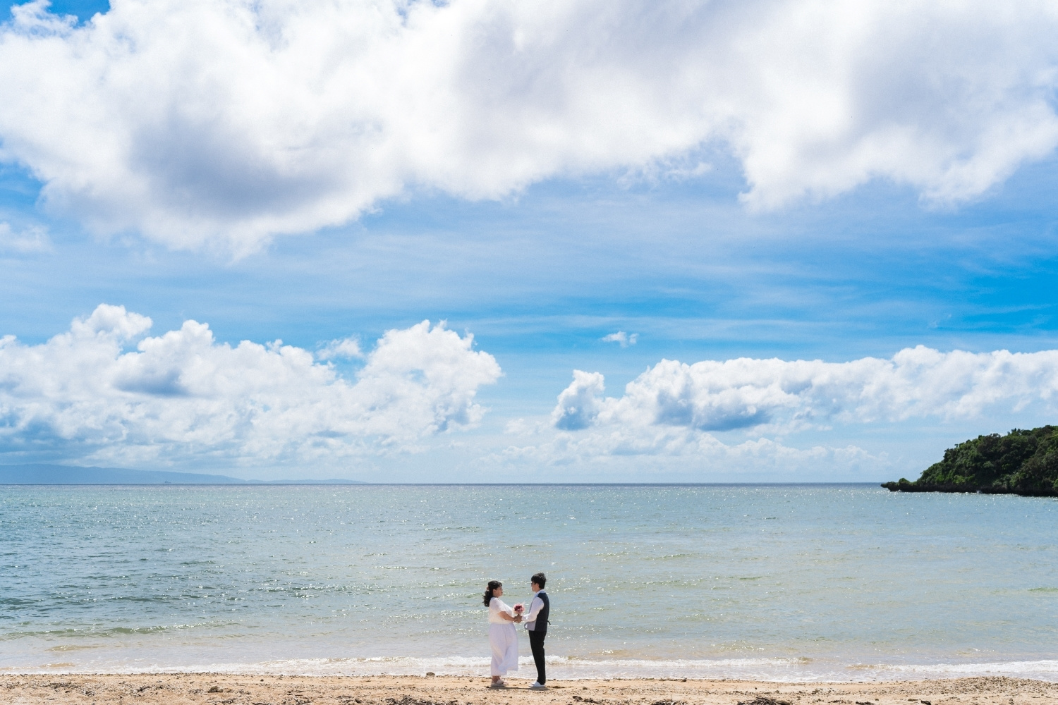 青空と海を背景に向かい合う新郎新婦