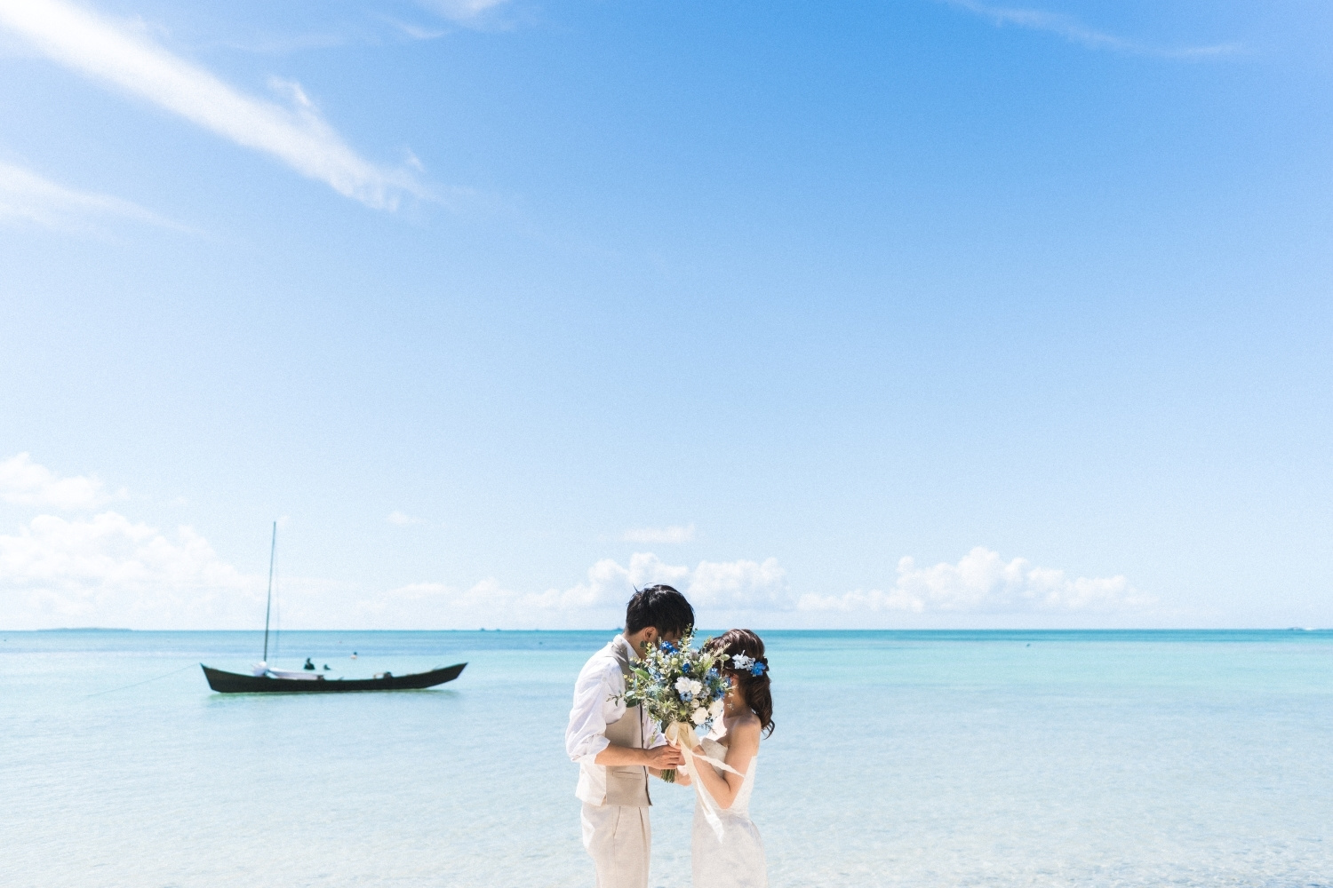 サバニ船が浮かぶ竹富島の海を背景に向かい合う新郎新婦