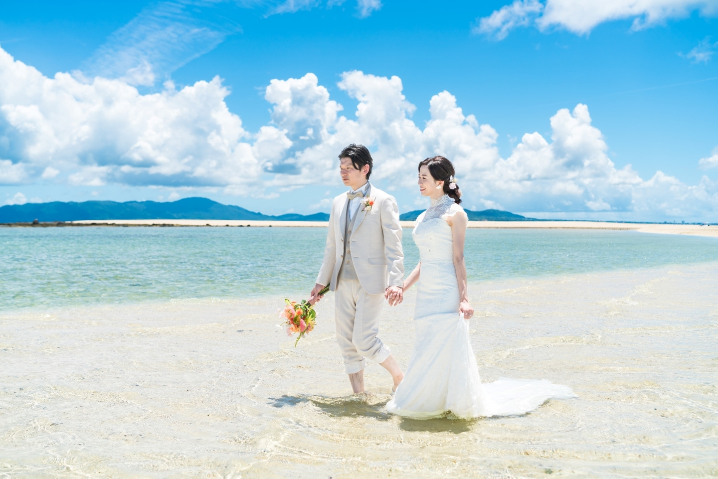 ビーチにある岩場で手を繋いで立つ新郎新婦
