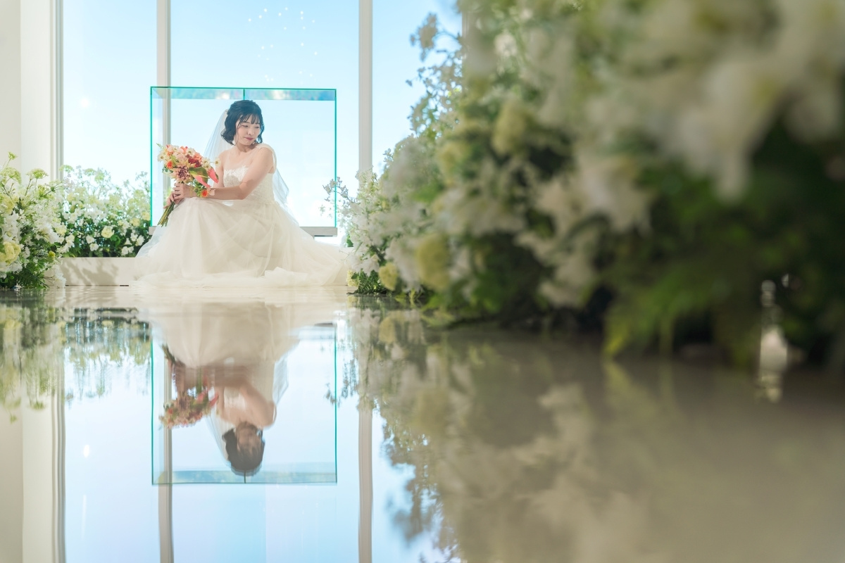 青空が見えるチャペルでブーケを持って座る新婦