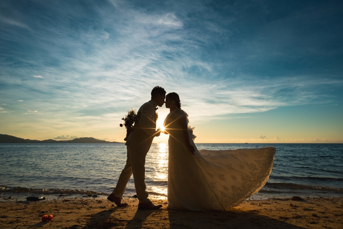 ビーチにある大きな木の下で抱き合う新郎新婦