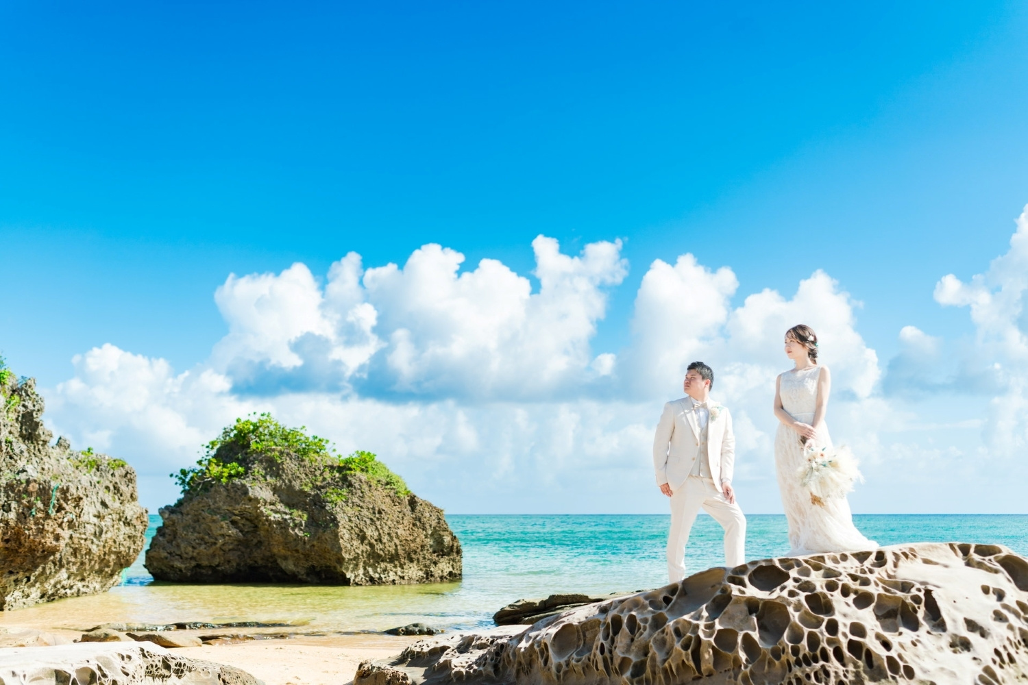 青い海と空をバックに岩場に立つ新郎新婦