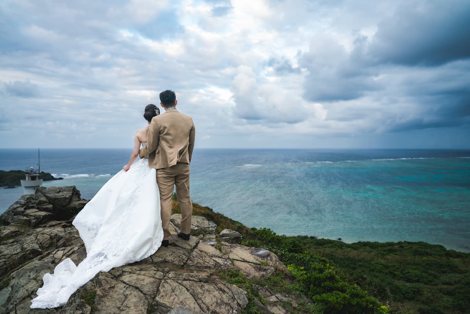 崖の上から海を眺める新郎新婦の後ろ姿