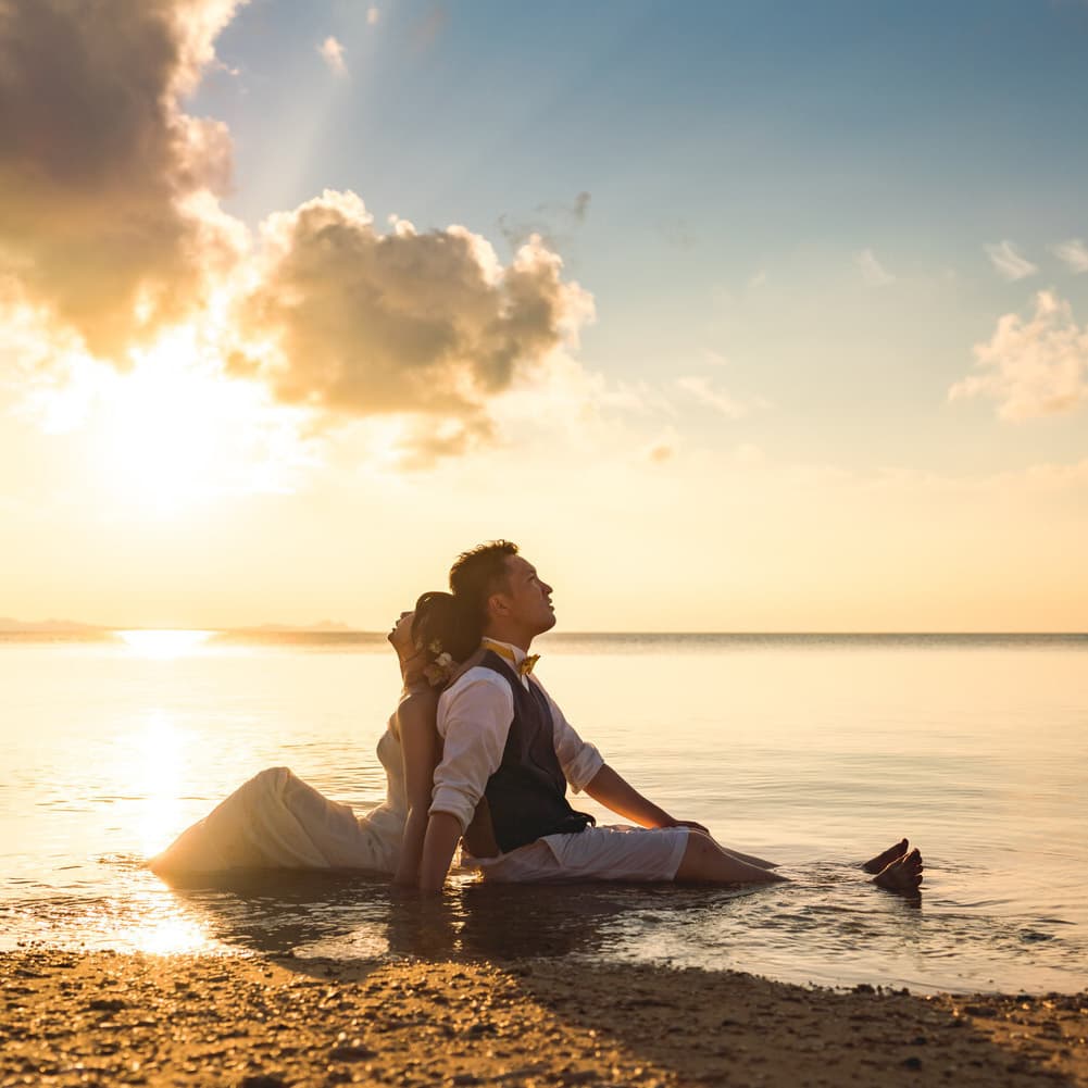 石垣島の海に沈む夕日を背景に背中合わせで座る新郎新婦