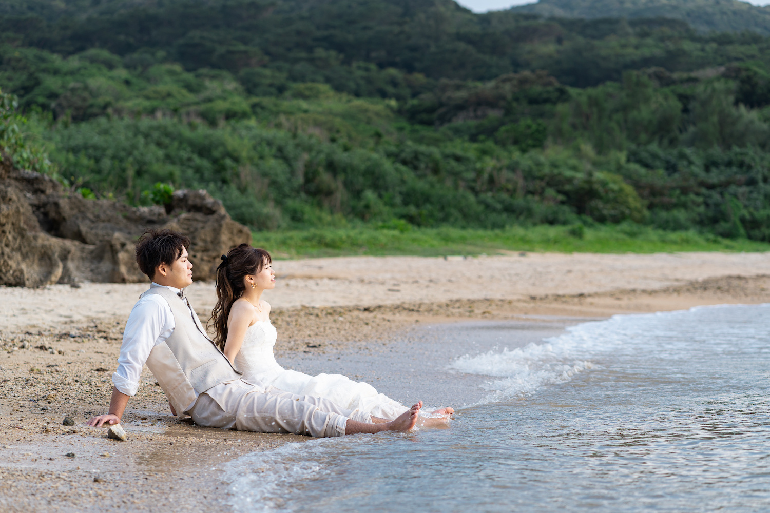 波打ち際に座って海を眺める新郎新婦