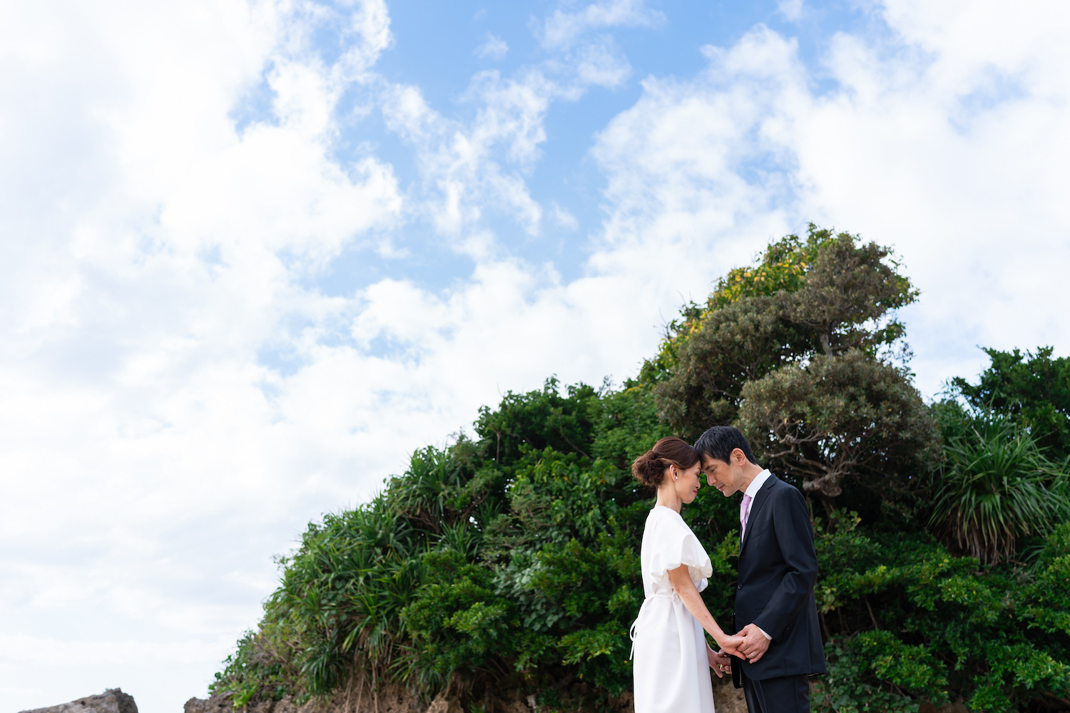 青空と緑を背景に顔を寄せ合う新郎新婦