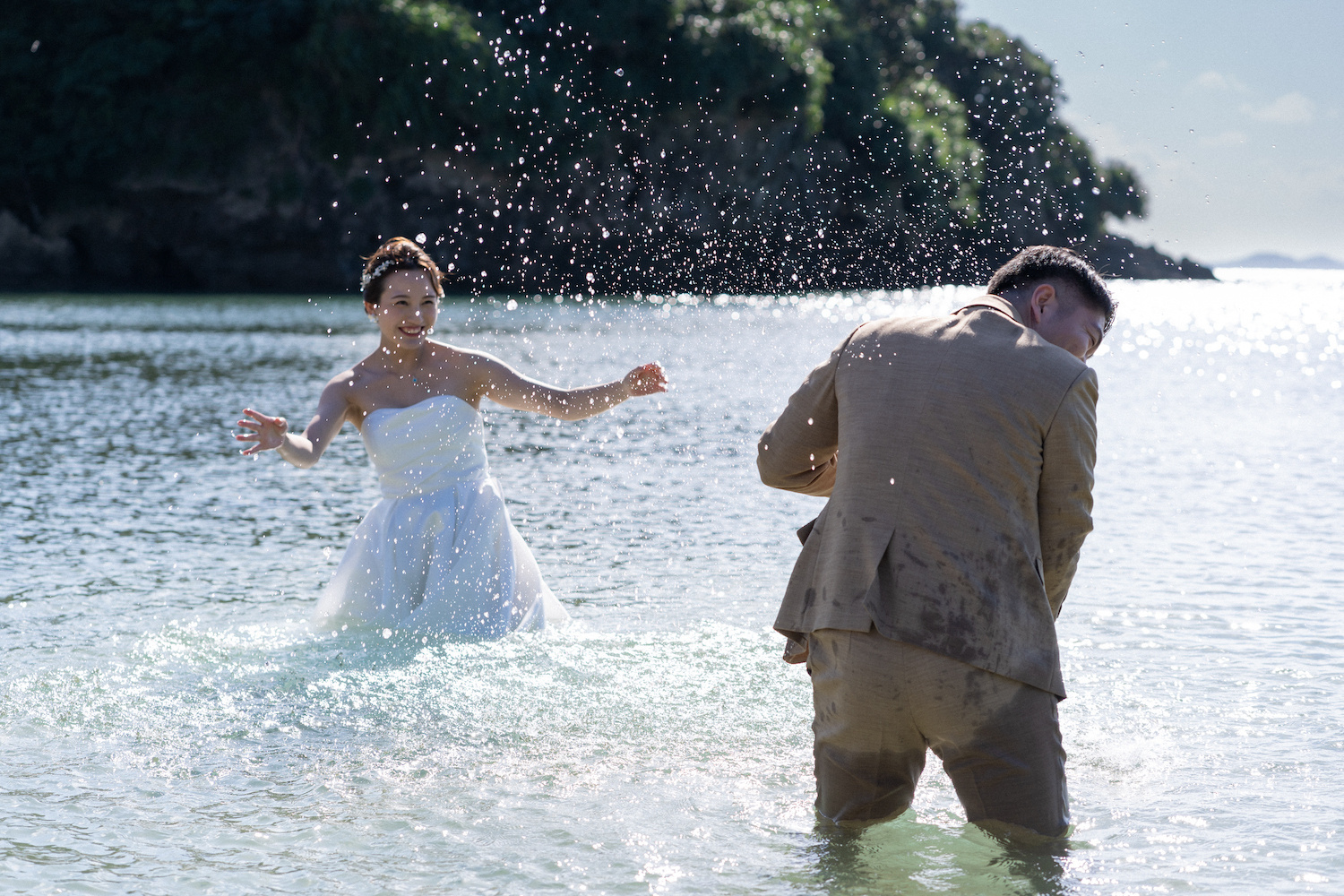 海に入って水をかけ合う新郎新婦