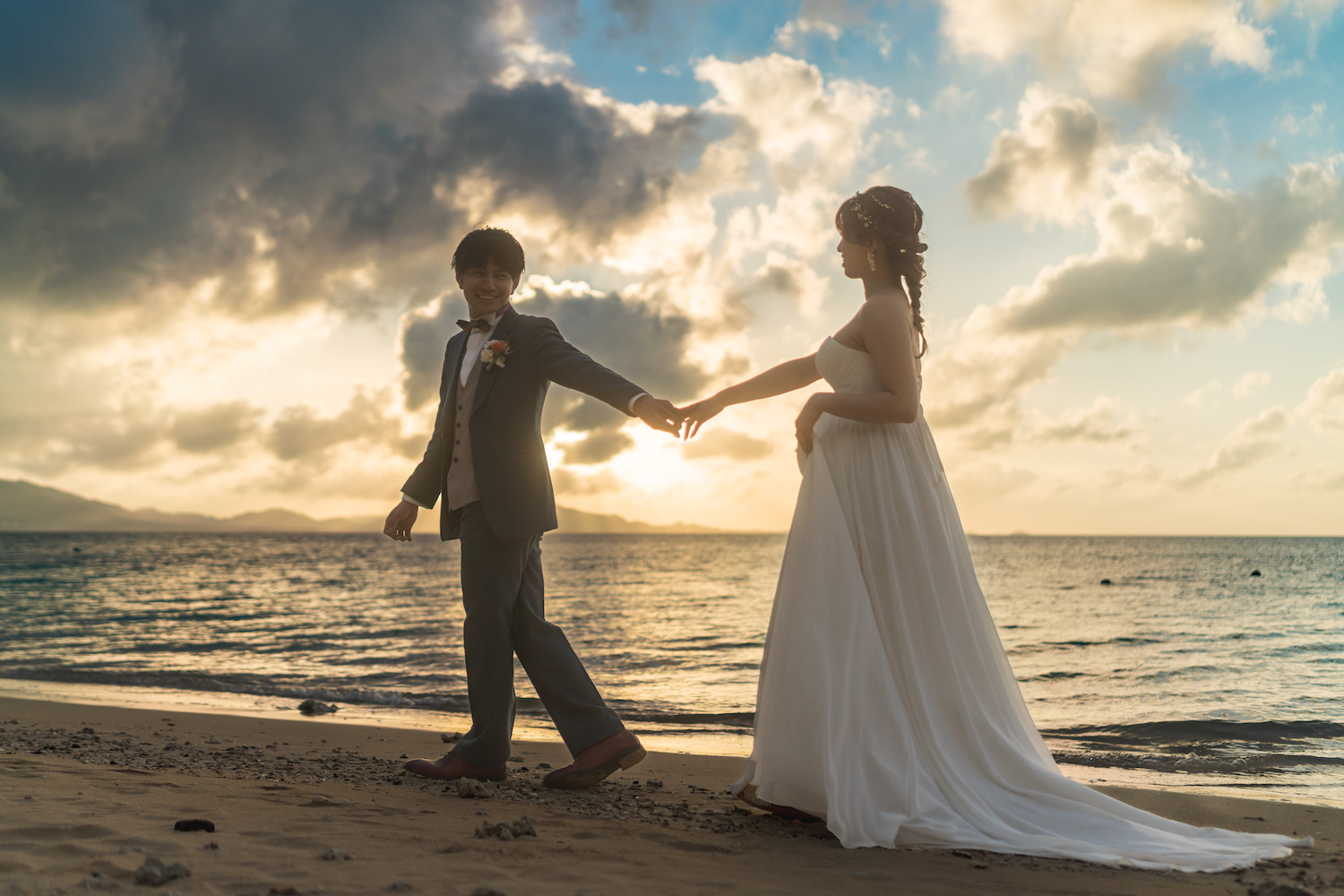 夕焼けに染まる海を背景に新婦の手を引く新郎