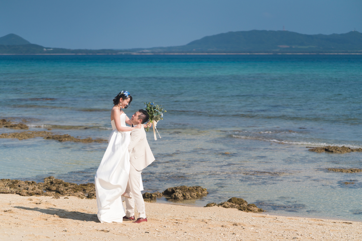 海を背景に新婦を抱き上げる新郎