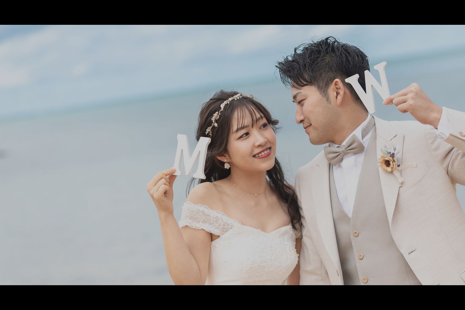 石垣島の海を背景にイニシャルを掲げて見つめ合う新郎新婦