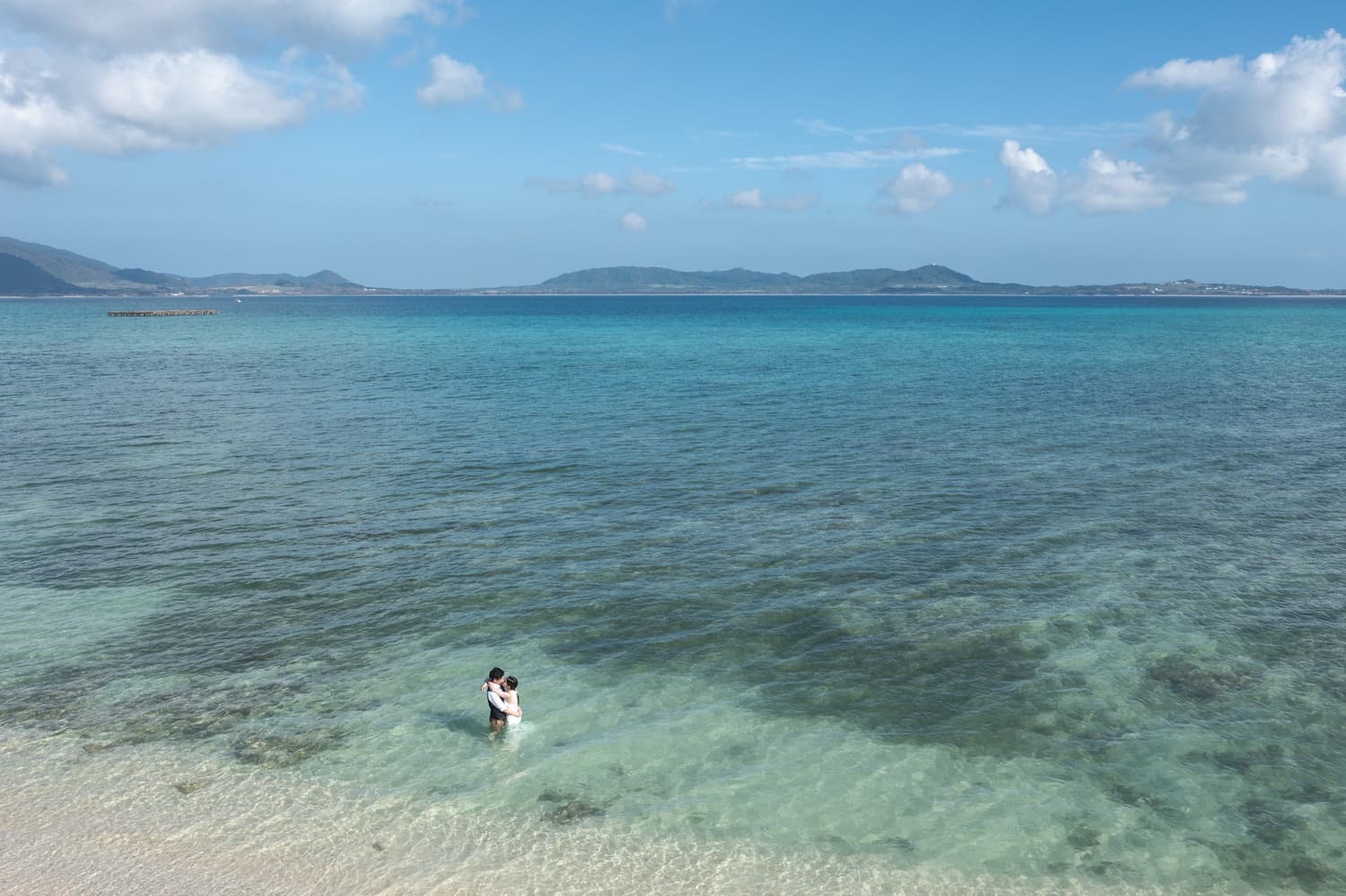 海に入って抱き合う新郎新婦のドローン写真