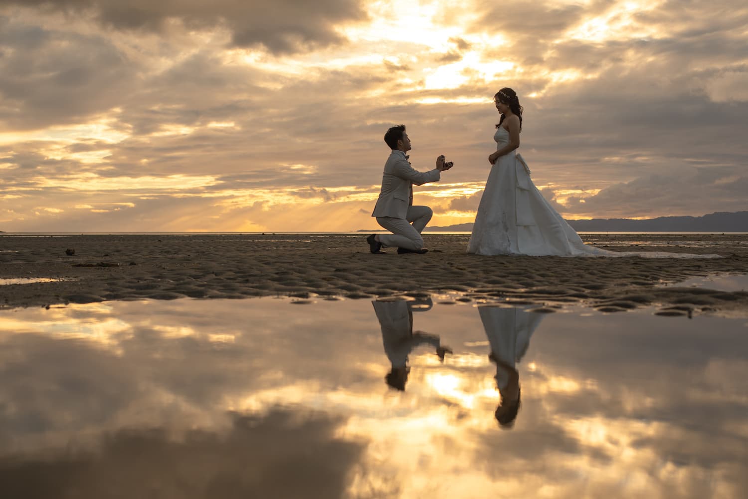 夕焼けに染まる海で新婦へプロポーズする新郎