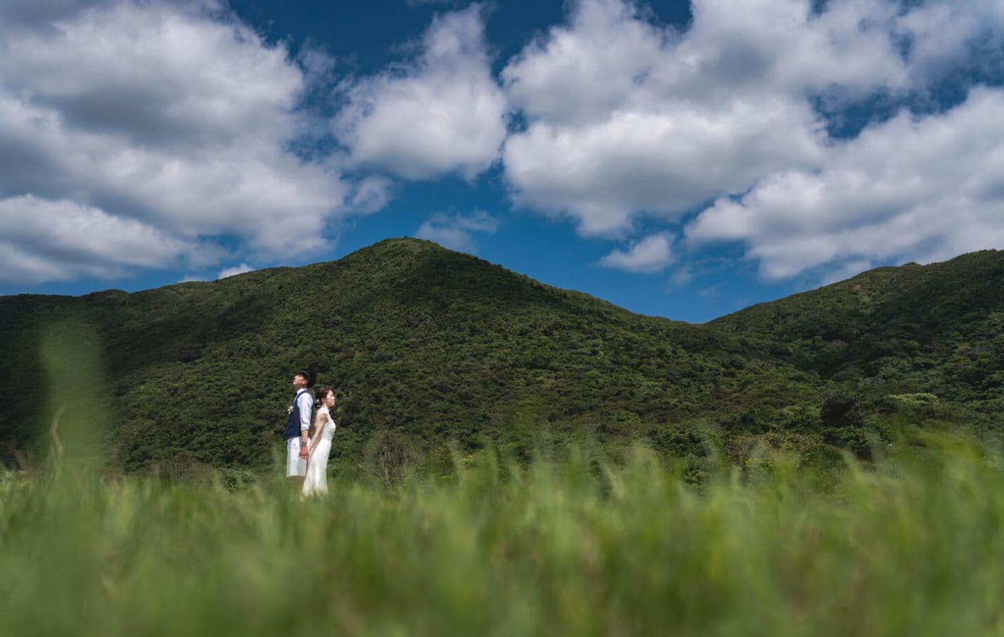 西表島の山を背景に背中合わせに立つ新郎新婦