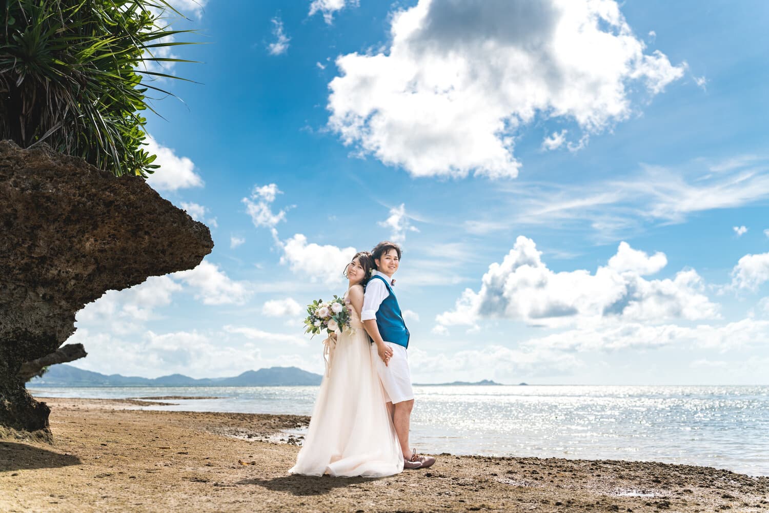 ビーチで青空を背景に背中合わせで立つ新郎新婦