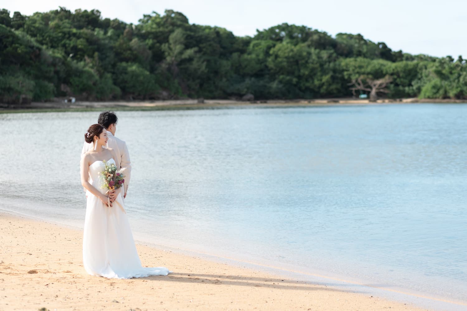 浜辺に背中合わせに立ち海を眺める新郎新婦