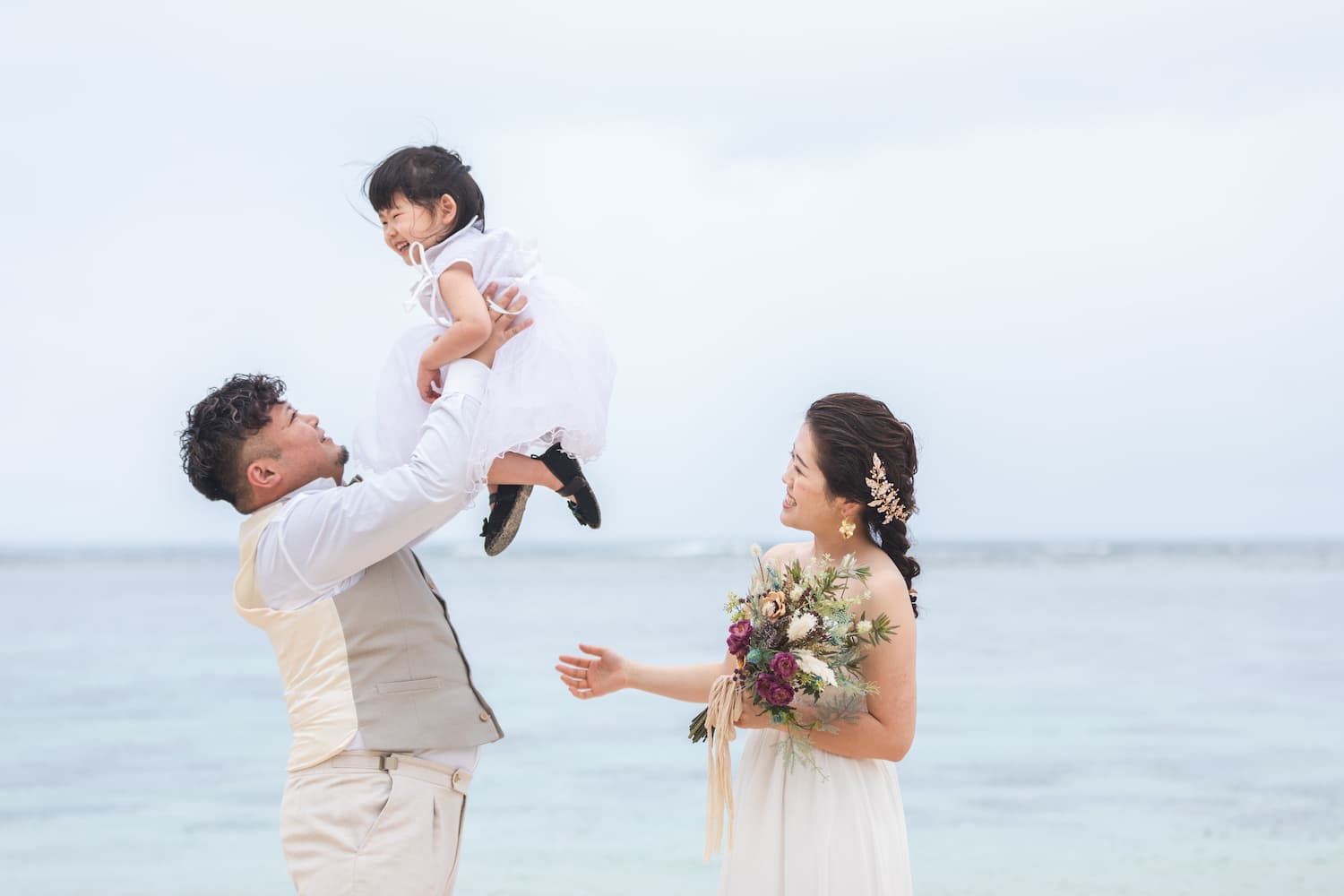 海を背景に子供を抱き上げる新郎と新婦