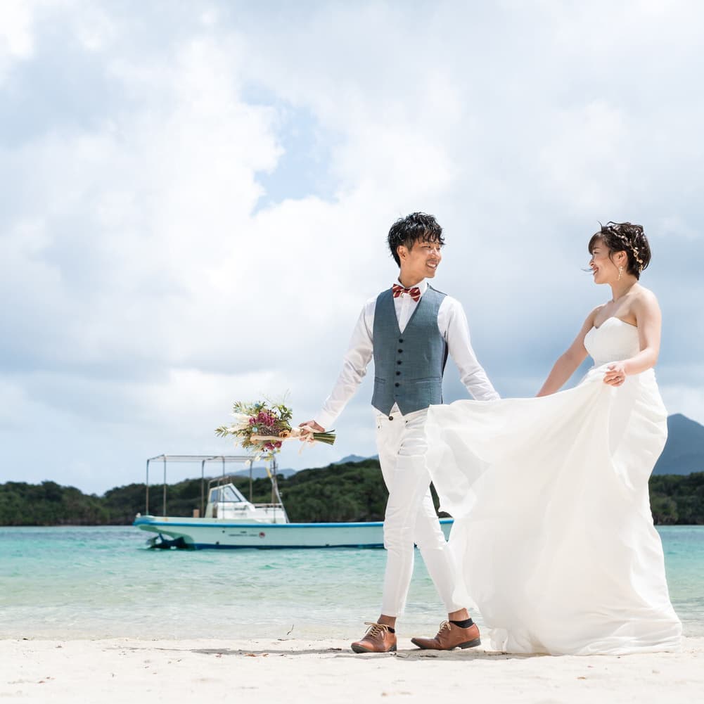 川平湾の海を背景に手を繋いで歩く新郎新婦