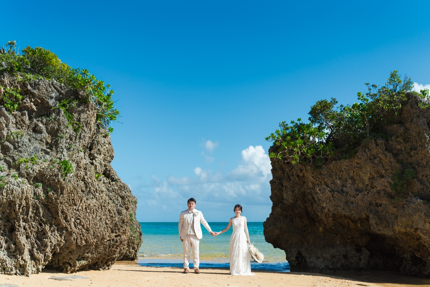 岩場に囲まれた海で手を繋いで立つ新郎新婦